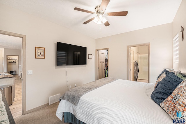 bedroom with ceiling fan, light carpet, visible vents, baseboards, and a walk in closet