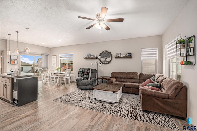 living room with ceiling fan, light wood-style flooring, and a textured ceiling