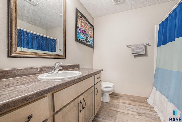 bathroom with a textured ceiling, toilet, wood finished floors, visible vents, and vanity