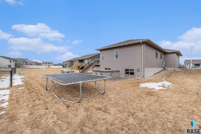 rear view of house featuring a trampoline, a residential view, fence, and a hot tub