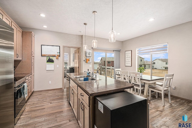 kitchen featuring a kitchen island with sink, a sink, hanging light fixtures, light wood-type flooring, and dark countertops