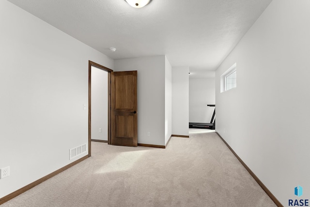 empty room featuring light carpet, a textured ceiling, visible vents, and baseboards