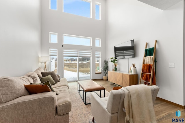 living area featuring baseboards, plenty of natural light, a towering ceiling, and light wood finished floors