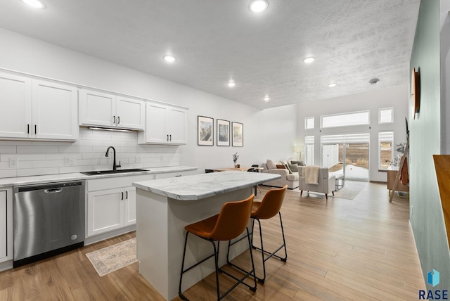 kitchen featuring dishwasher, a kitchen island, open floor plan, white cabinetry, and a sink