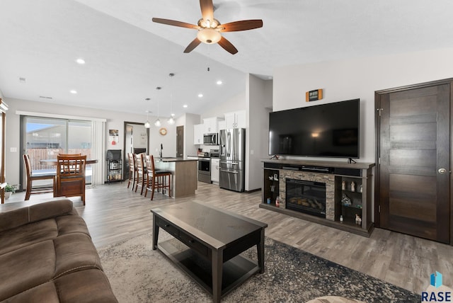 living area with a ceiling fan, vaulted ceiling, a stone fireplace, light wood-type flooring, and recessed lighting