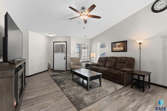 living room featuring ceiling fan, baseboards, vaulted ceiling, and wood finished floors