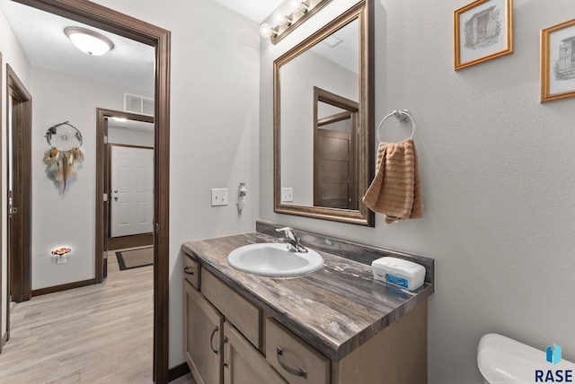 bathroom featuring toilet, wood finished floors, vanity, visible vents, and baseboards