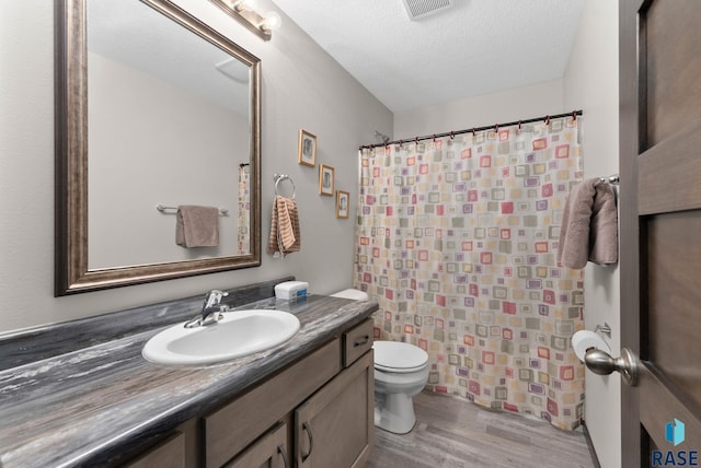 bathroom featuring visible vents, toilet, vanity, a textured ceiling, and wood finished floors