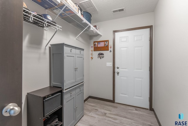 interior space with light wood-type flooring, visible vents, a textured ceiling, and baseboards