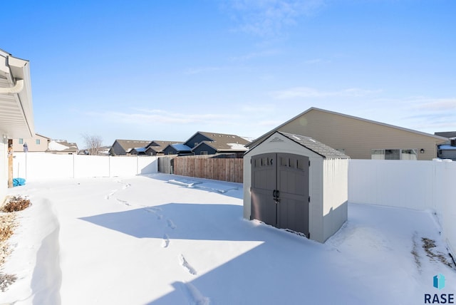 yard layered in snow with an outbuilding, a fenced backyard, and a storage unit