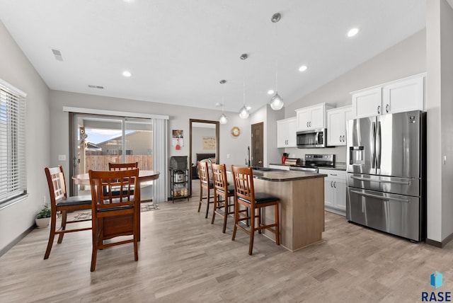 kitchen with a kitchen island, decorative light fixtures, stainless steel appliances, a kitchen bar, and white cabinetry