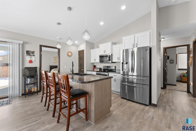 kitchen with appliances with stainless steel finishes, decorative light fixtures, a kitchen island with sink, white cabinetry, and a sink