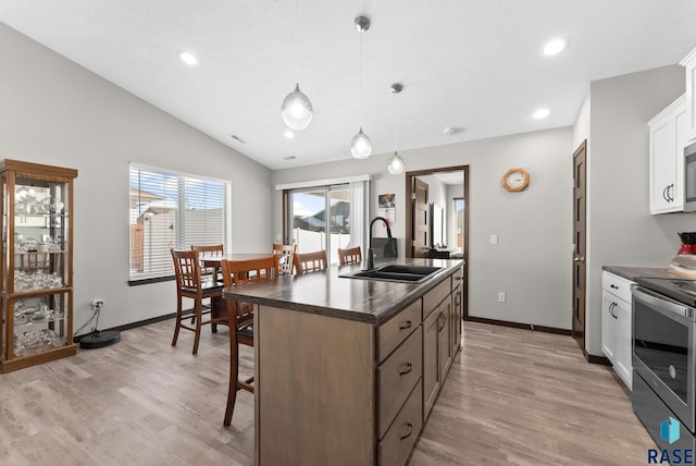 kitchen featuring white cabinets, dark countertops, a kitchen island with sink, stainless steel appliances, and a sink