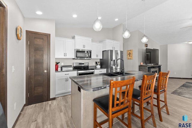 kitchen featuring stainless steel appliances, dark countertops, hanging light fixtures, white cabinetry, and a kitchen breakfast bar