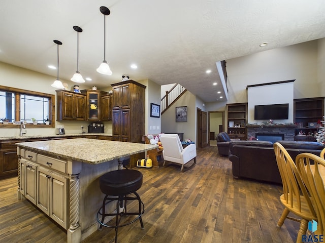 kitchen with dark wood finished floors, glass insert cabinets, a kitchen island, a sink, and light stone countertops