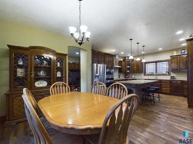 dining space featuring arched walkways, a notable chandelier, dark wood finished floors, recessed lighting, and a textured ceiling