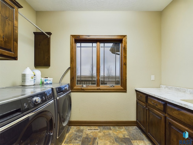 washroom featuring a textured ceiling, baseboards, cabinet space, stone finish floor, and washing machine and clothes dryer