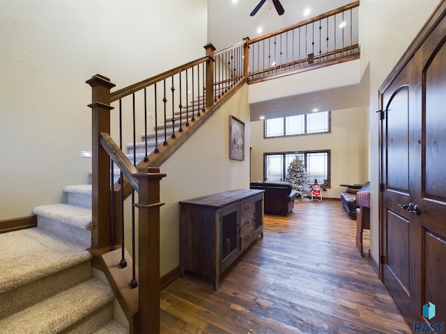 staircase featuring ceiling fan, wood finished floors, a towering ceiling, and baseboards