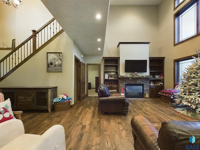 living room featuring a stone fireplace, a high ceiling, and wood finished floors