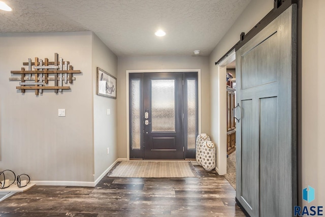 entryway featuring a textured ceiling, a barn door, dark wood-style flooring, and baseboards