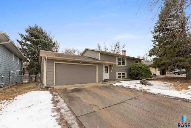 tri-level home with a garage, a chimney, fence, and concrete driveway