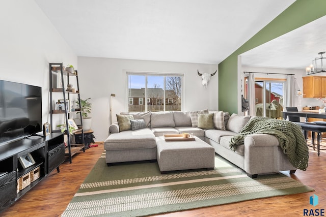 living area featuring vaulted ceiling, plenty of natural light, wood finished floors, and a notable chandelier