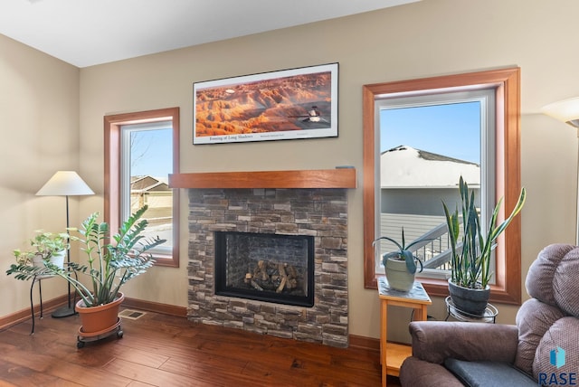 living area with a stone fireplace, wood finished floors, visible vents, and baseboards