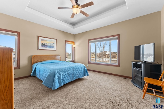 bedroom featuring ceiling fan, light carpet, visible vents, baseboards, and a tray ceiling