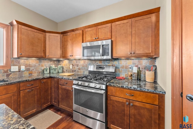 kitchen with tasteful backsplash, dark wood finished floors, dark stone counters, appliances with stainless steel finishes, and brown cabinets