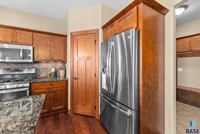 kitchen with brown cabinetry, decorative backsplash, dark stone counters, dark wood-style flooring, and stainless steel appliances