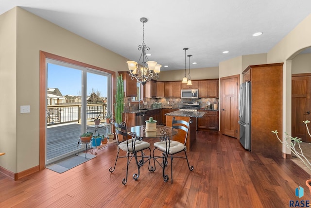 dining area with arched walkways, dark wood-style flooring, a chandelier, and baseboards