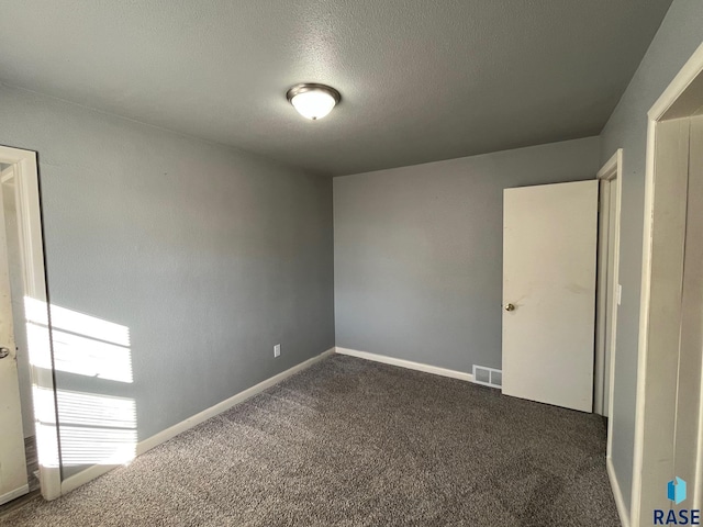 unfurnished bedroom with baseboards, visible vents, dark colored carpet, and a textured ceiling