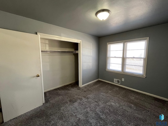 unfurnished bedroom with baseboards, visible vents, dark carpet, and a closet