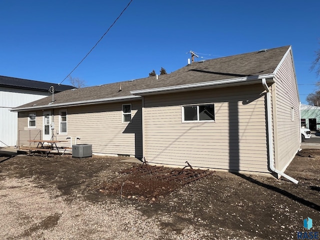 rear view of house featuring central AC and roof with shingles