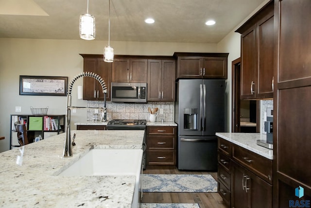 kitchen featuring light stone counters, dark wood-style flooring, hanging light fixtures, decorative backsplash, and appliances with stainless steel finishes