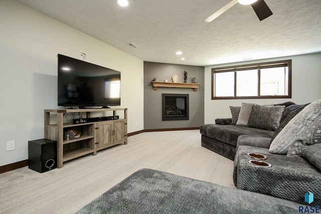 living area with a textured ceiling, a glass covered fireplace, a ceiling fan, and baseboards