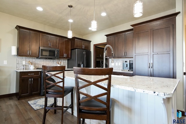 kitchen with an island with sink, stainless steel microwave, hanging light fixtures, a kitchen bar, and refrigerator with ice dispenser