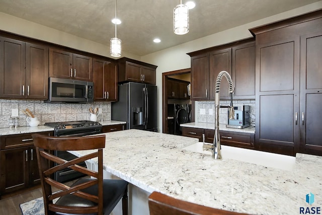 kitchen featuring pendant lighting, stainless steel microwave, washing machine and dryer, dark brown cabinetry, and refrigerator with ice dispenser