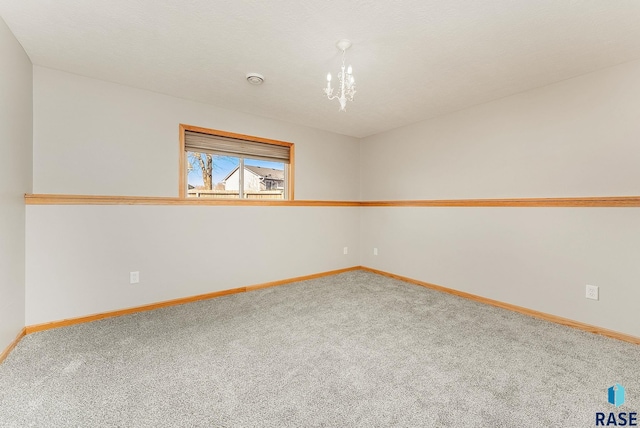 unfurnished room with carpet floors, baseboards, and a notable chandelier