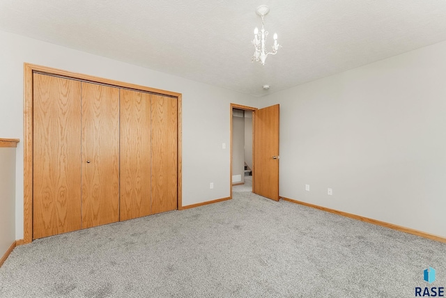 unfurnished bedroom featuring a notable chandelier, a closet, light carpet, a textured ceiling, and baseboards