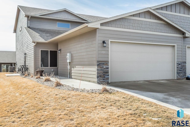 view of front of house with an attached garage, stone siding, driveway, and a shingled roof