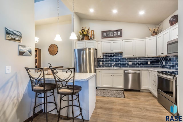 kitchen with a breakfast bar area, stainless steel appliances, light countertops, light wood-type flooring, and a sink