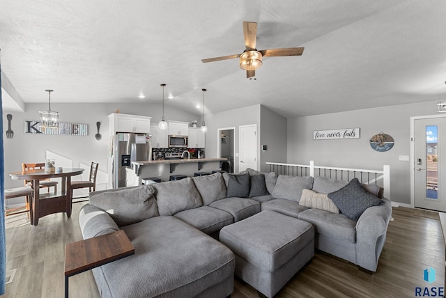 living area with dark wood finished floors, lofted ceiling, a textured ceiling, baseboards, and ceiling fan with notable chandelier