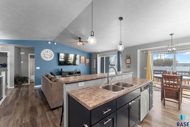 kitchen featuring hanging light fixtures, open floor plan, a kitchen island with sink, a sink, and dishwasher