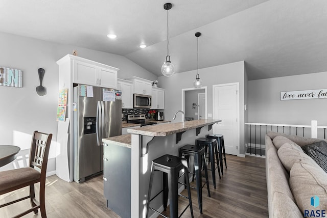 kitchen with a center island with sink, white cabinets, a breakfast bar area, decorative light fixtures, and stainless steel appliances