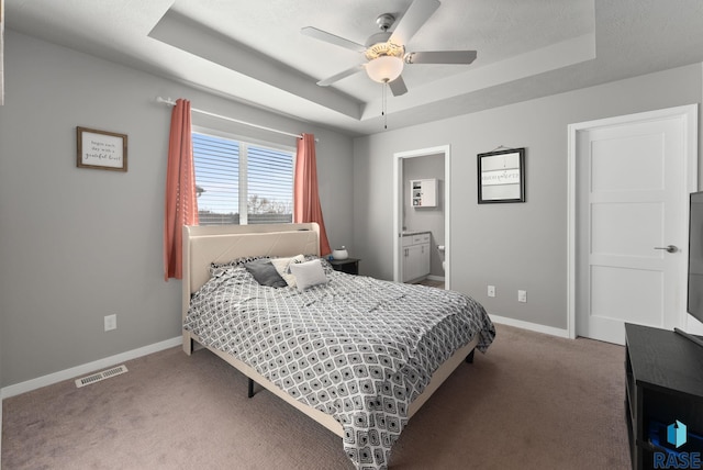 carpeted bedroom featuring a tray ceiling, visible vents, and baseboards