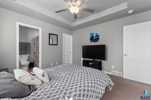 carpeted bedroom featuring baseboards, visible vents, a raised ceiling, a ceiling fan, and ensuite bathroom