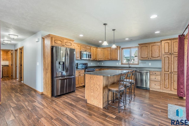 kitchen featuring dark wood finished floors, dark countertops, appliances with stainless steel finishes, a kitchen island, and a sink