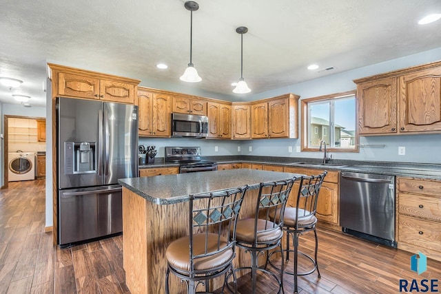 kitchen featuring washer / dryer, dark countertops, a kitchen island, stainless steel appliances, and a sink