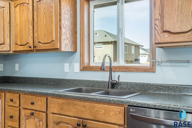 kitchen with brown cabinetry, dark countertops, a sink, and dishwashing machine